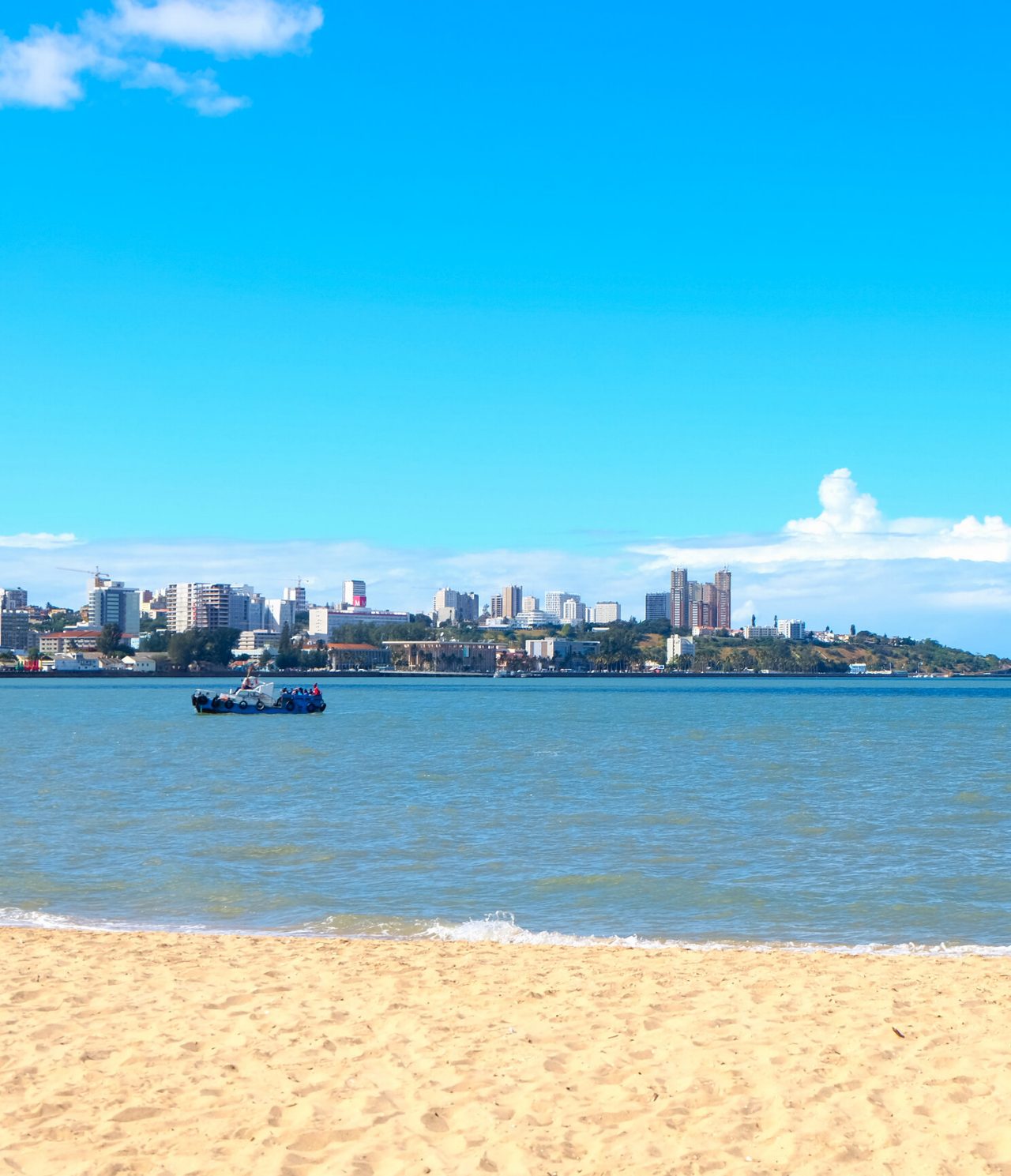 Vue sur la ville de Maputo depuis l'autre côté du fleuve, sur une plage où plusieurs enfants jouent avec l'eau