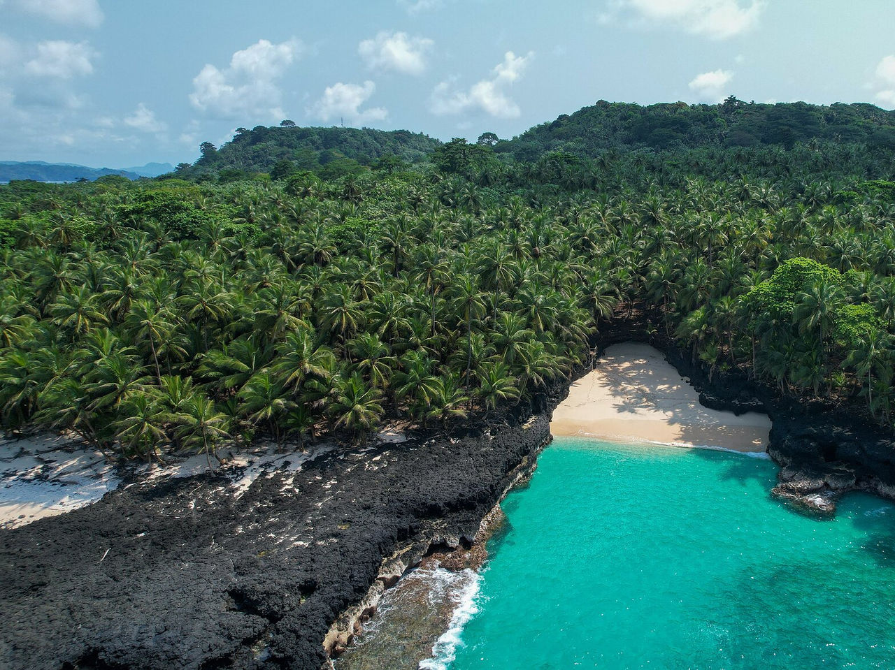 Plage déserte avec des rochers volcaniques autour, eau cristalline et des palmiers entourant la plage