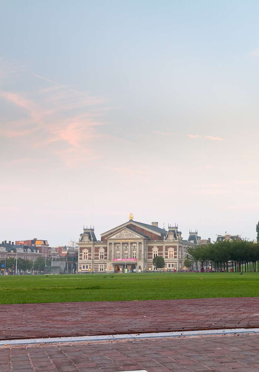 Vue de l'herbe et de la zone pavée du Museumplein à Amsterdam avec des arbres alignés et le bâtiment du musée en arrière-plan