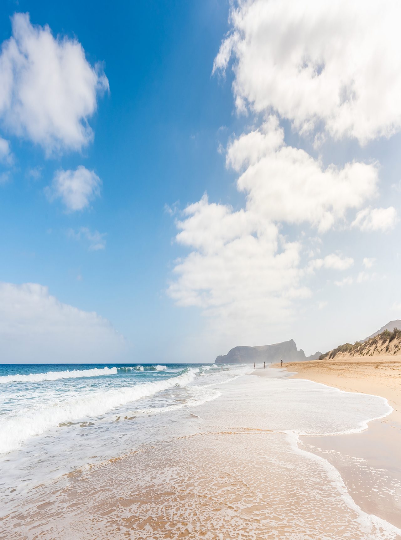 Plage étendue à Porto Santo avec du sable clair, des vagues calmes et un ciel bleu avec quelques nuages