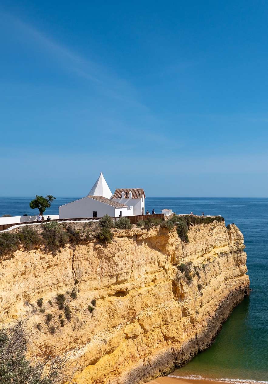 Vue sur la falaise de la plage Senhora da Rocha, avec une petite maison blanche surplombant la falaise et une mer calme