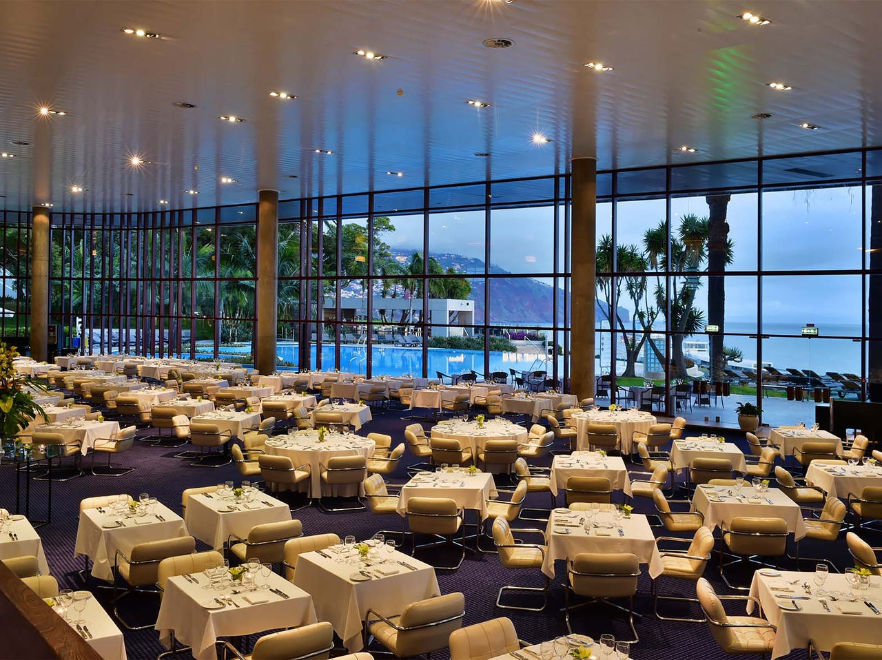 Le restaurant Panorâmico de l’hôtel à Funchal, sur l’île de Madère, a plusieurs tables et chaises rembourrées beige