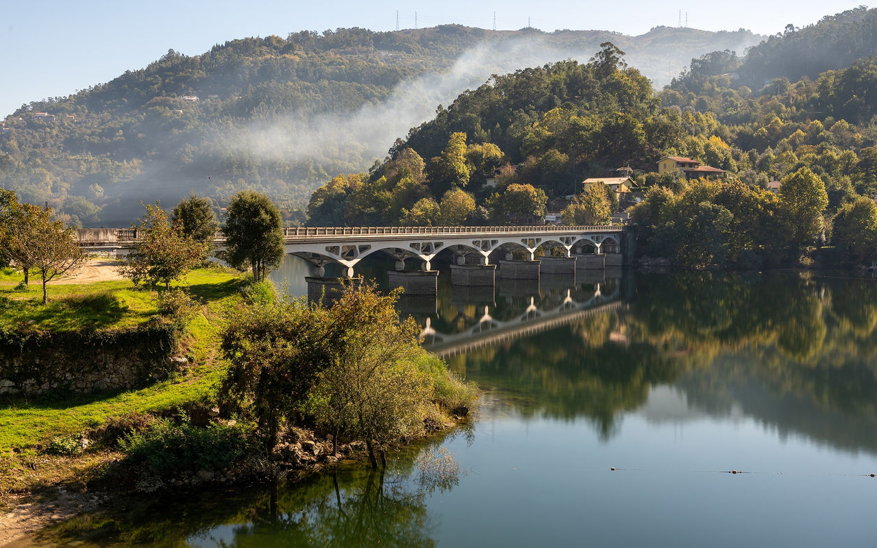 Paysage du nord du Portugal avec un pont de pierre sur une rivière, entouré de collines verdoyantes