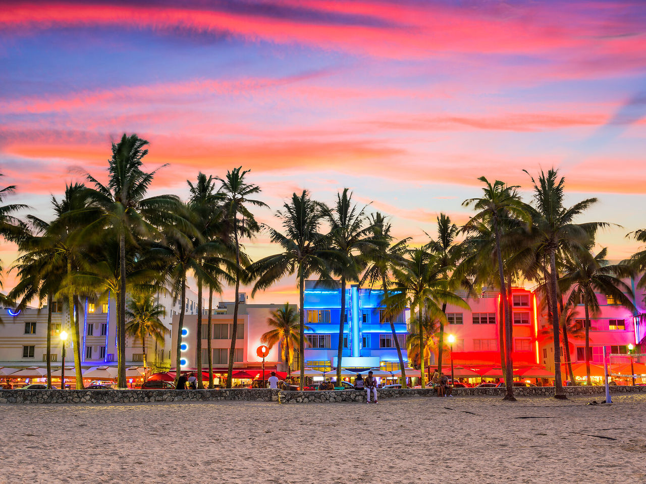Coucher de soleil vibrant à Miami Beach, avec des palmiers en silhouette et des bâtiments Art déco illuminés