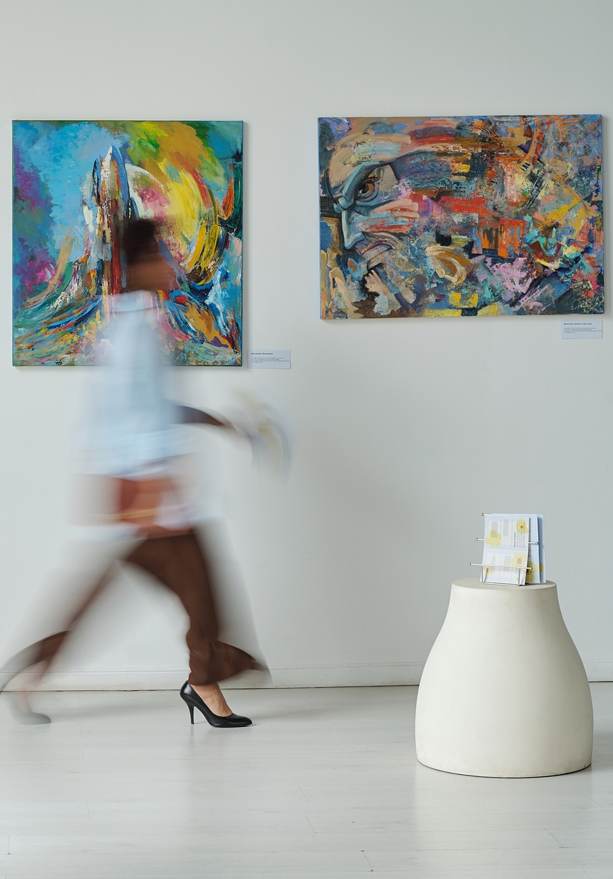 Exposition d'art avec des peintures abstraites colorées sur les murs et deux personnes marchant devant les œuvres