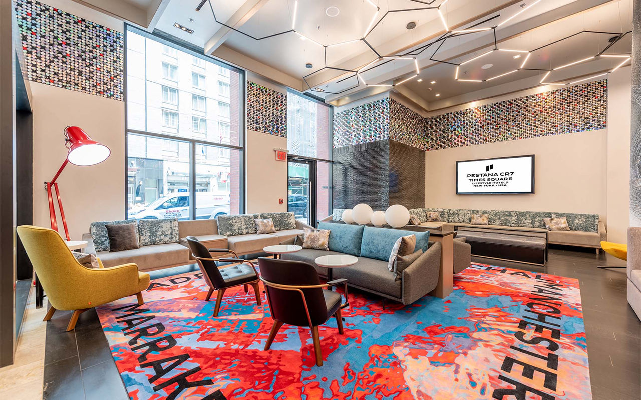 Vue intérieure du hall du Pestana CR7 Times Square, avec des canapés confortables, des chaises et un tapis coloré