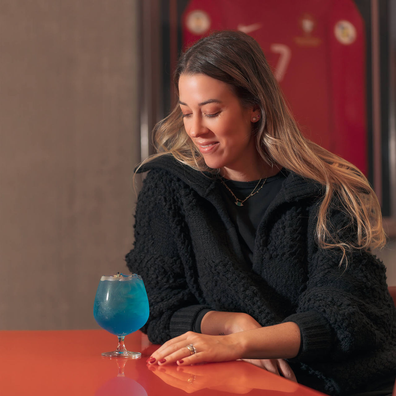 Fille buvant un cocktail, assise à une table, avec le maillot de Cristiano Ronaldo accroché au mur