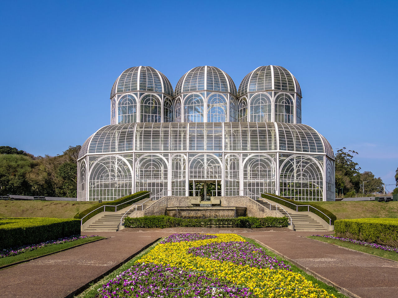 Vue frontale de l'imposante serre du Jardin Botanique de Curitiba avec ses jardins fleuris et colorés