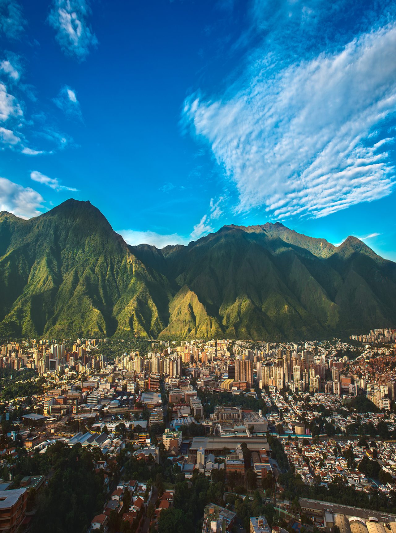Vue aérienne de la ville de Caracas, avec de hauts bâtiments, contrastant avec la nature montagneuse et le ciel bleu