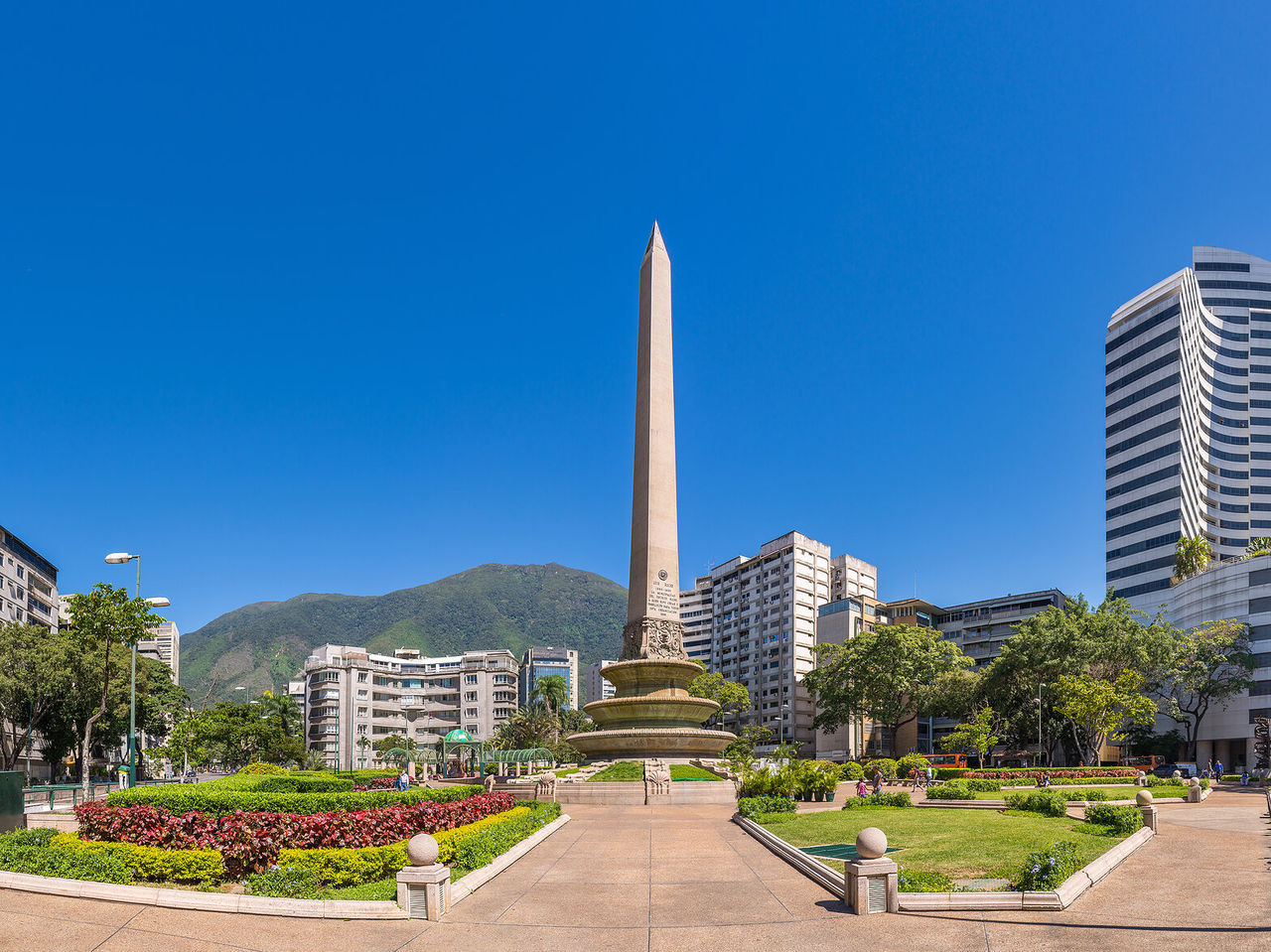 Monument Obélisque, grande colonne de pierre au milieu d'un parc avec des fleurs, entourée de hauts bâtiments à Caracas