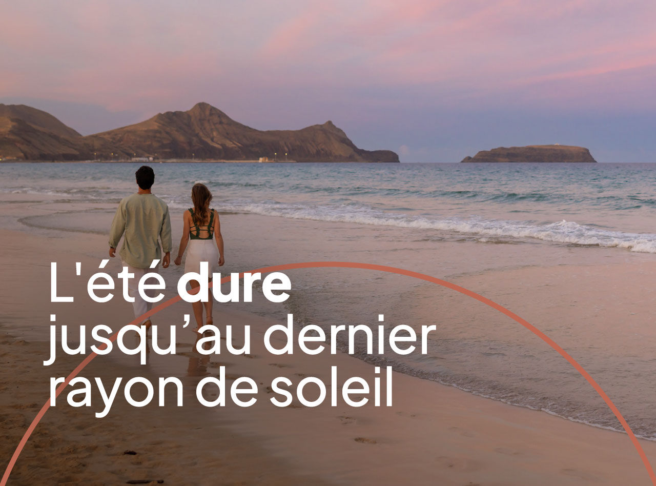 Couple marchant sur une plage au coucher du soleil avec montagnes rocheuses et vagues calmes en arrière-plan