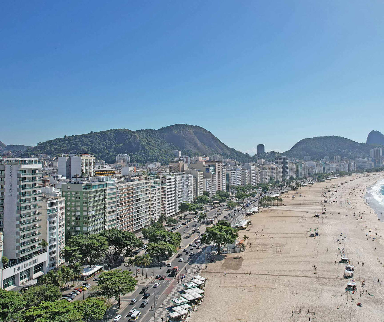 Rio de Janeiro hotel com vista para a praia extensa, avenida costeira e montanhas sob céu azul ao fundo