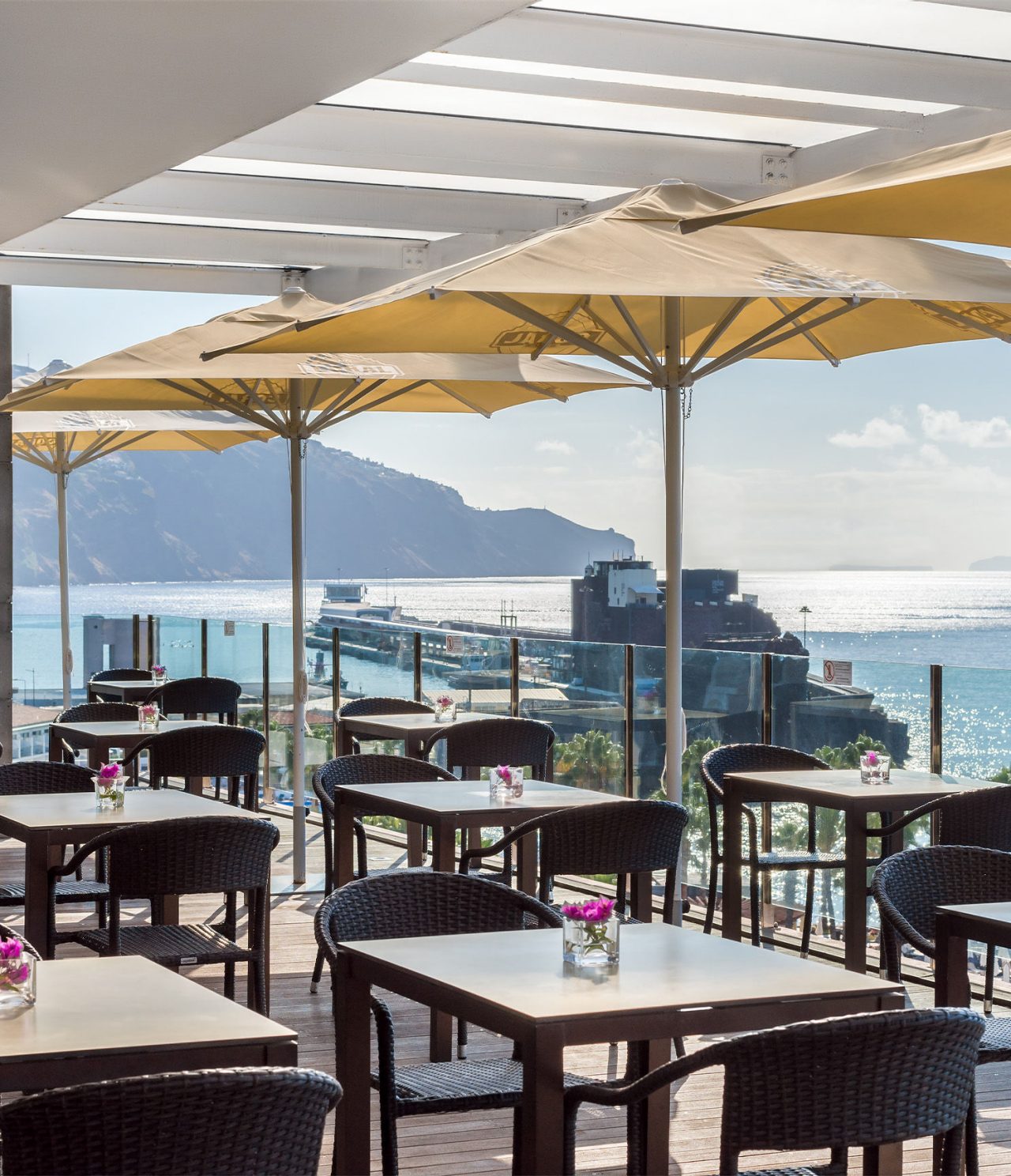 De Garden Pool-bar in het hotel in het centrum van Funchal, Madeira, heeft een terras met stoelen, tafels en uitzicht op zee
