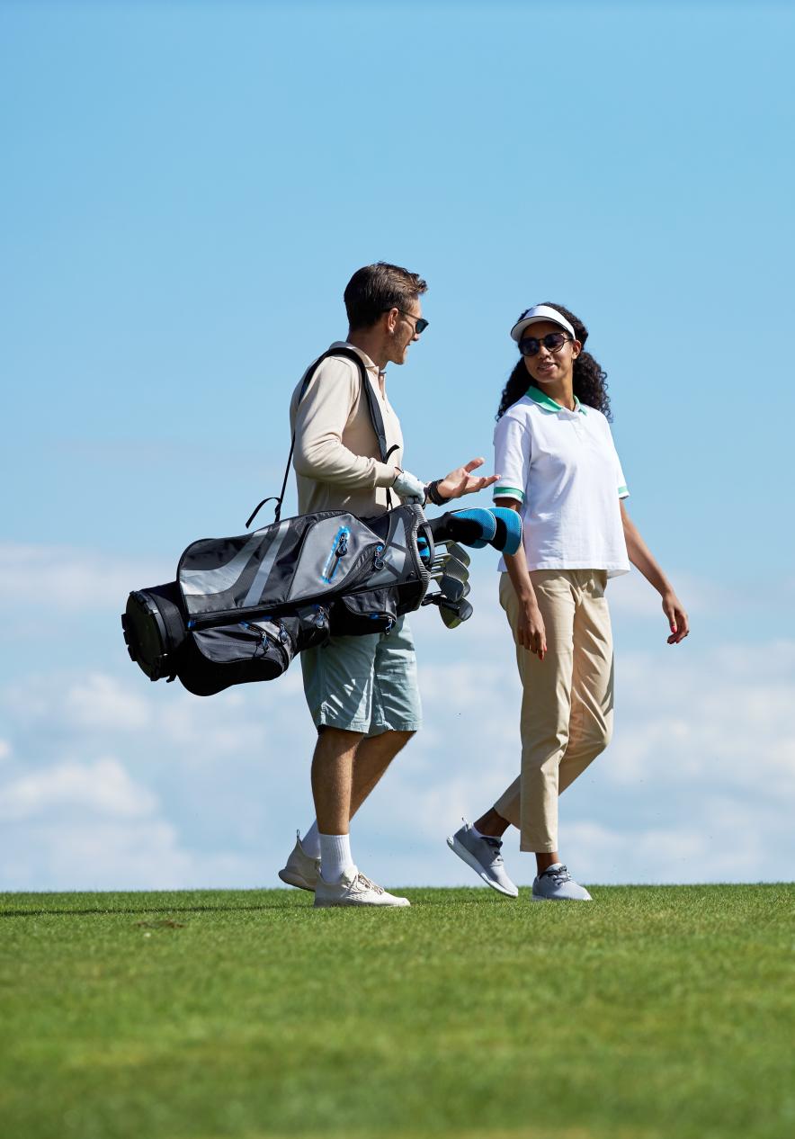 Een stel draagt golfclubs op een golfbaan op Porto Santo, met een blauwe lucht op de achtergrond