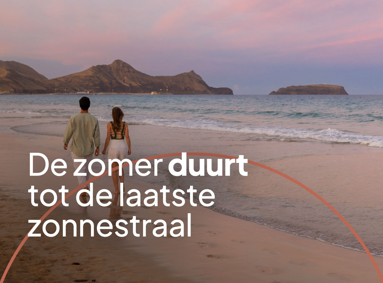 Stel wandelt hand in hand langs rustig strand bij zonsondergang met bergen, zachte golven en roze lucht