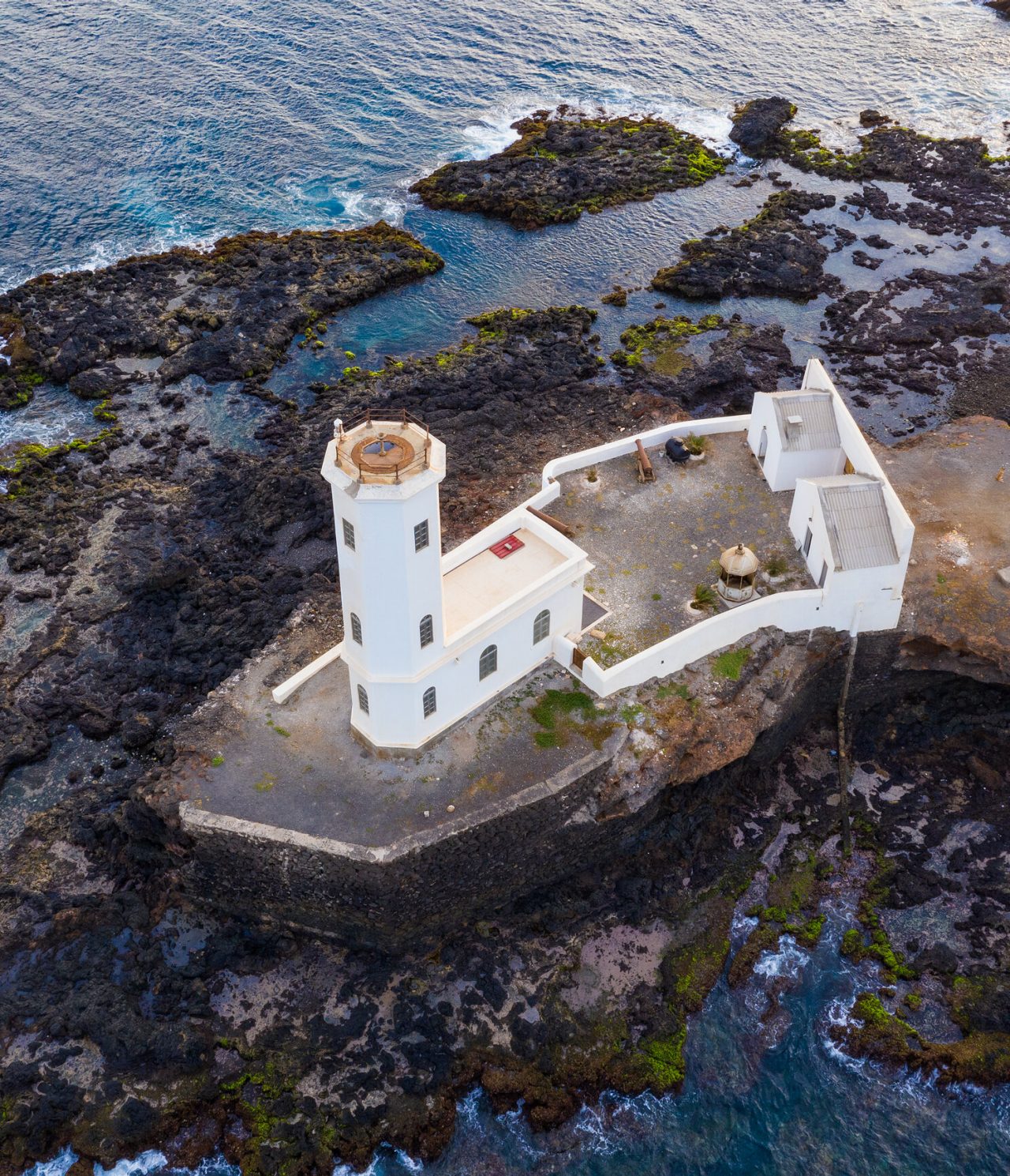 Explore Hotéis na Cidade da Praia com vista aérea de um farol branco junto à costa rochosa atlântica vulcânica