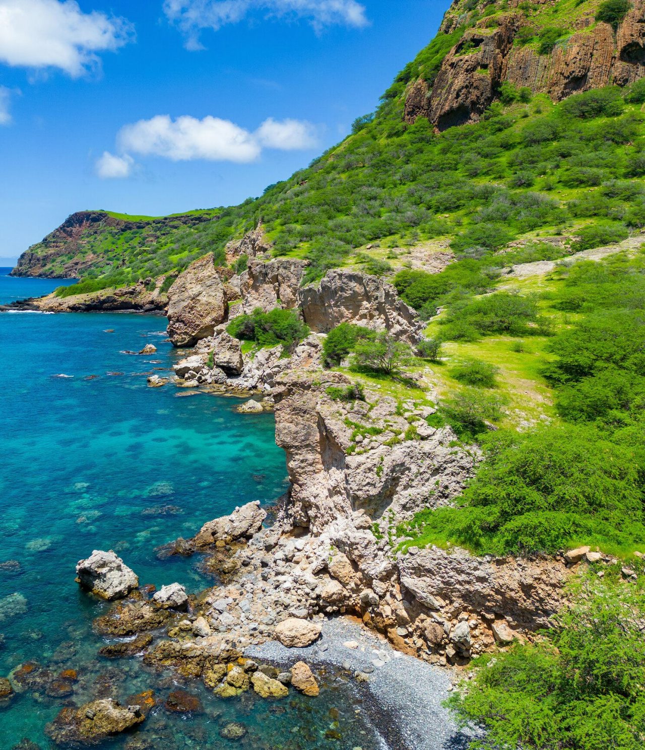 O azul do Oceano Atlântico em contraste com a natureza verdejante e rochosa da Cidade da Praia em Cabo Verde