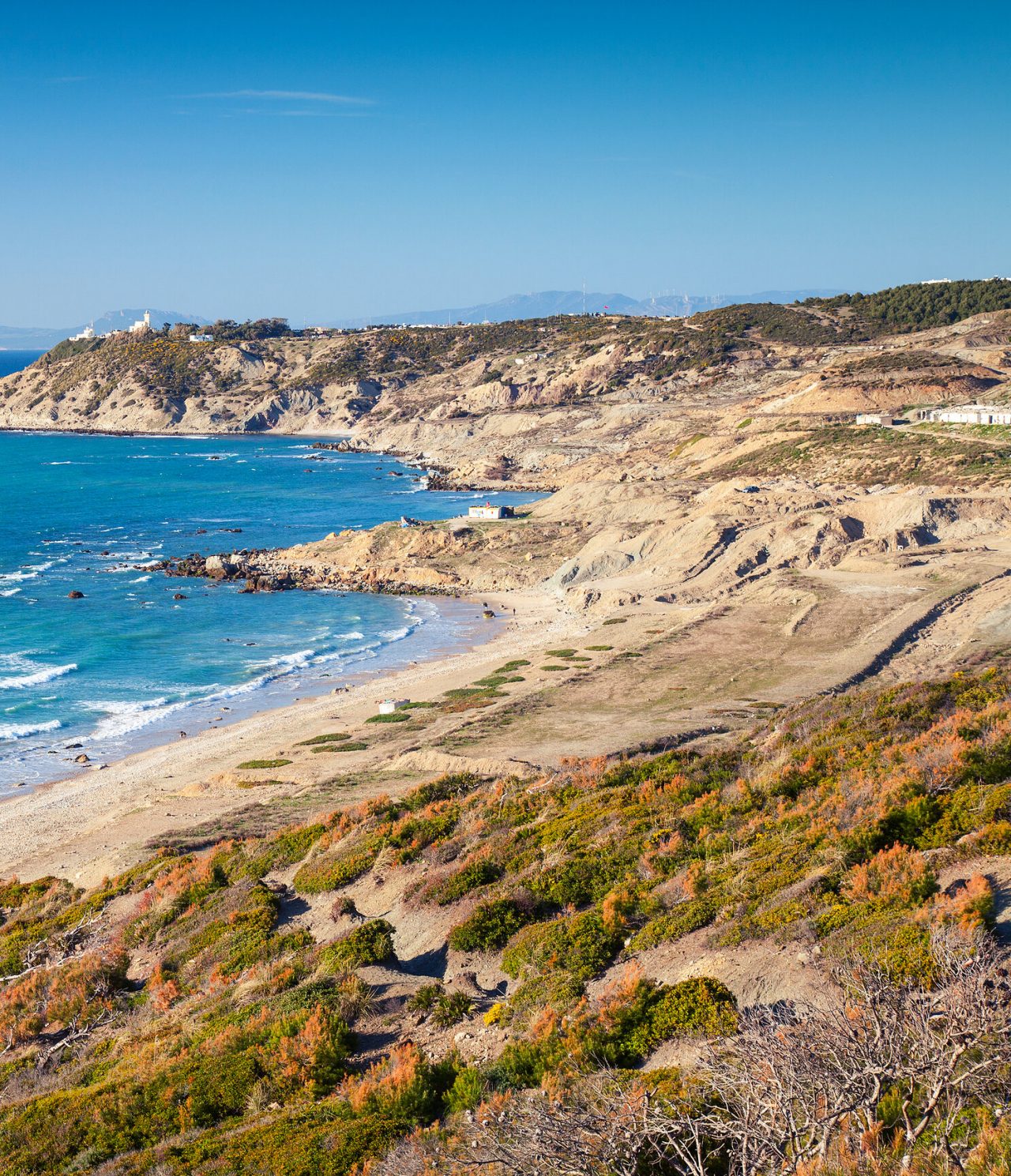 Explore Hotéis em Tânger com vista para a costa rochosa, praia extensa e mar azul sob céu limpo ao fundo