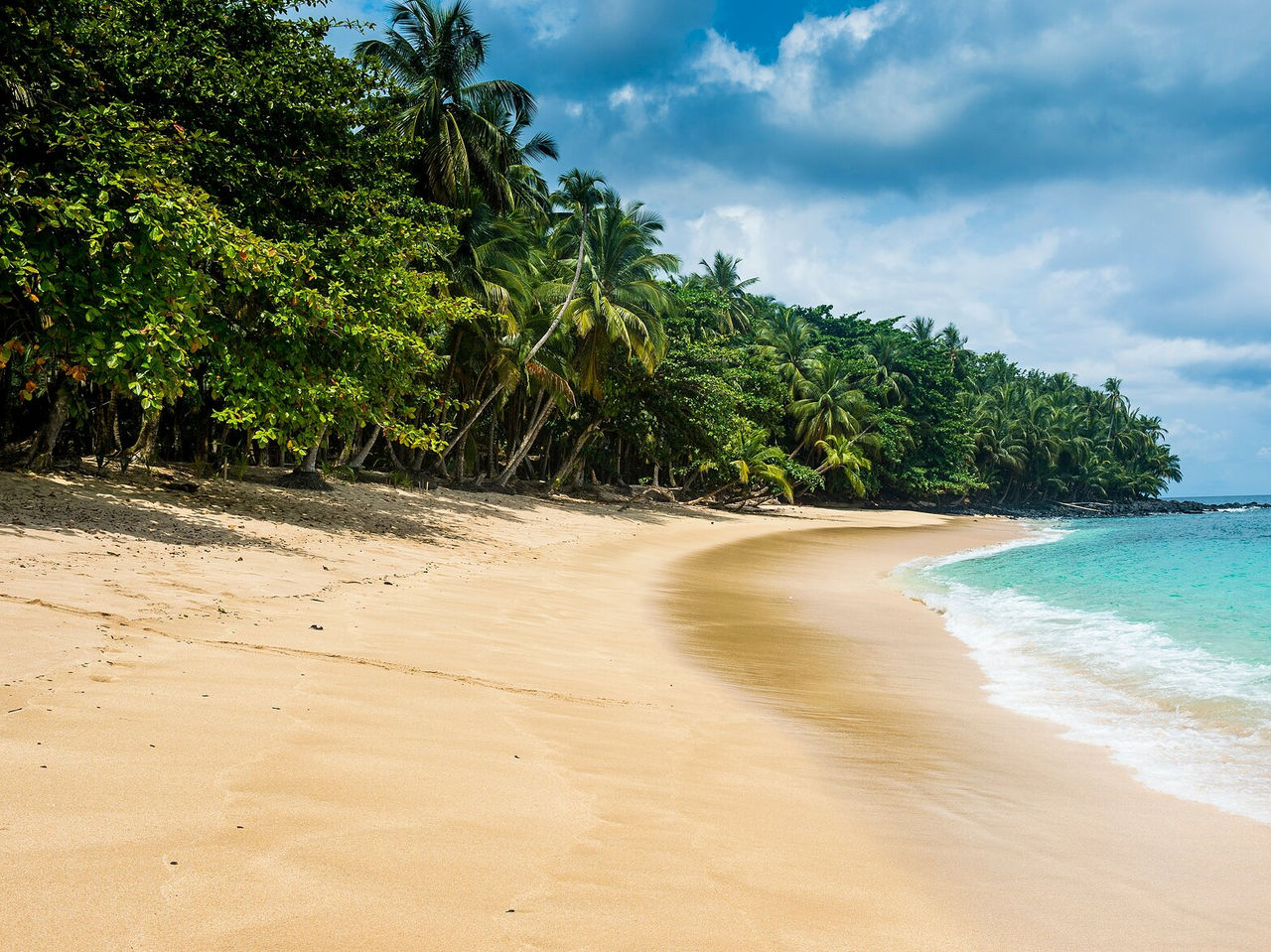 Explore Hotéis em São Tomé com vista para uma praia de areia clara, mar azul-turquesa e palmeiras densas