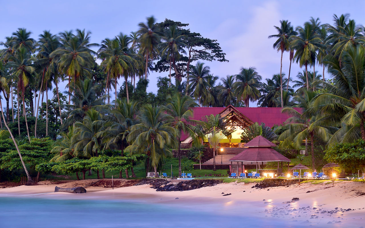 Praia e edifício com espreguiçadeiras e palmeiras do Pestana Equador, Hotel no Ilhéu das Rolas, em São Tomé