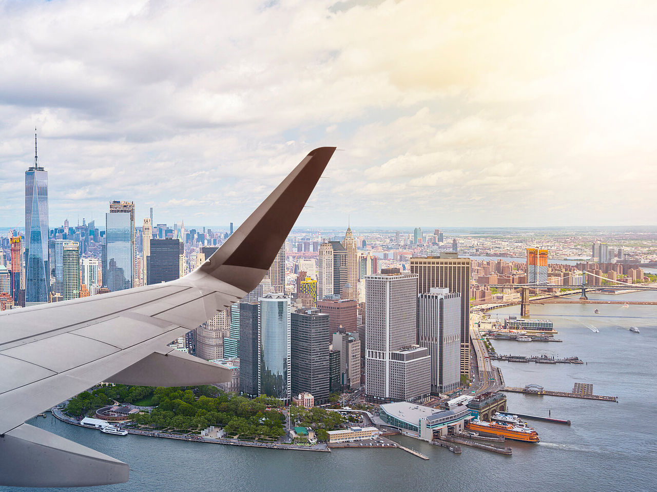Explore Hotéis em Nova Iorque com vista aérea sobre Manhattan e a asa de um avião junto ao rio Hudson ao entardecer