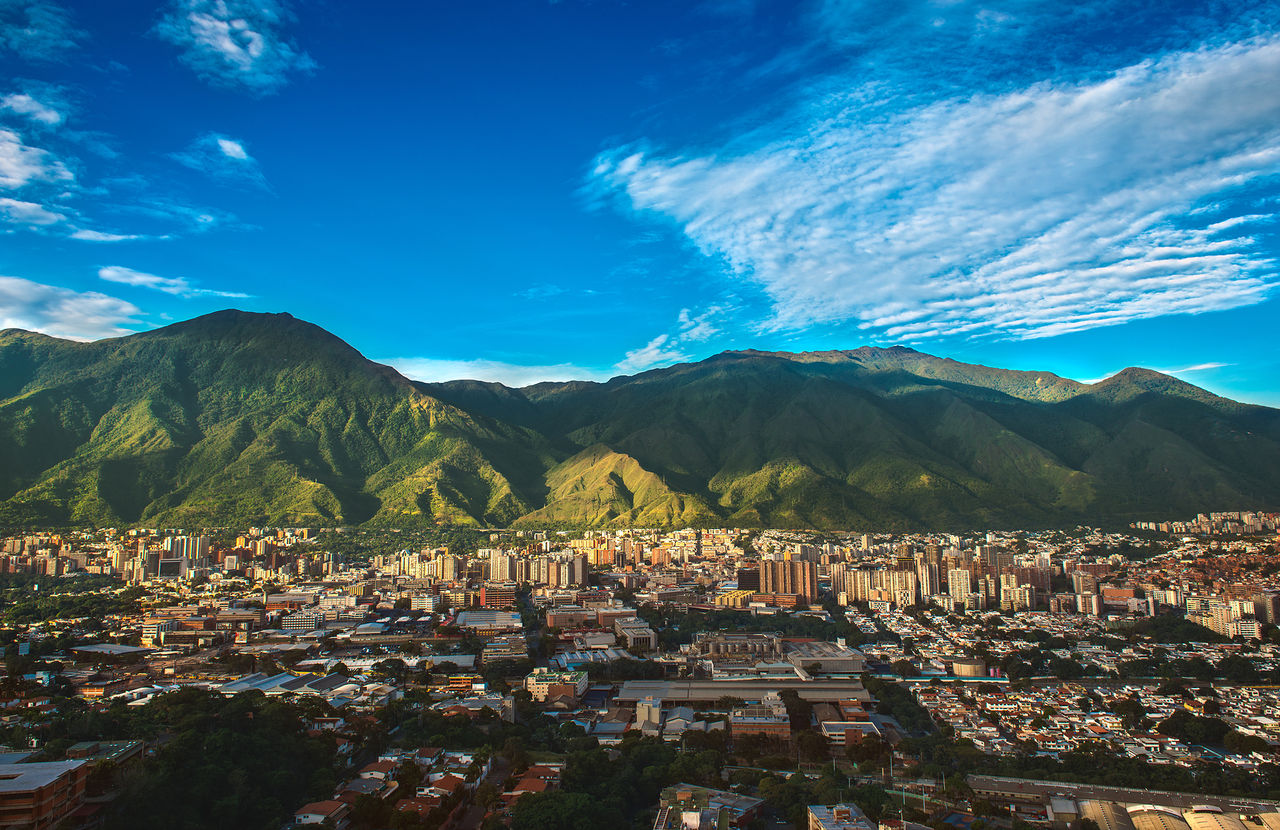 Vista aérea da cidade de Caracas, com prédios altos, contrastando com a natureza montanhosa, e o céu azul