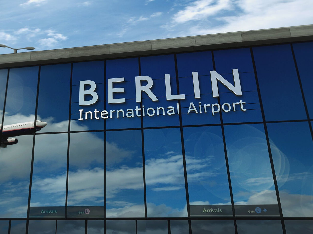 Fachada da zona de chegadas do aeroporto internacional de Berlin, com um avião refletido nos vidros