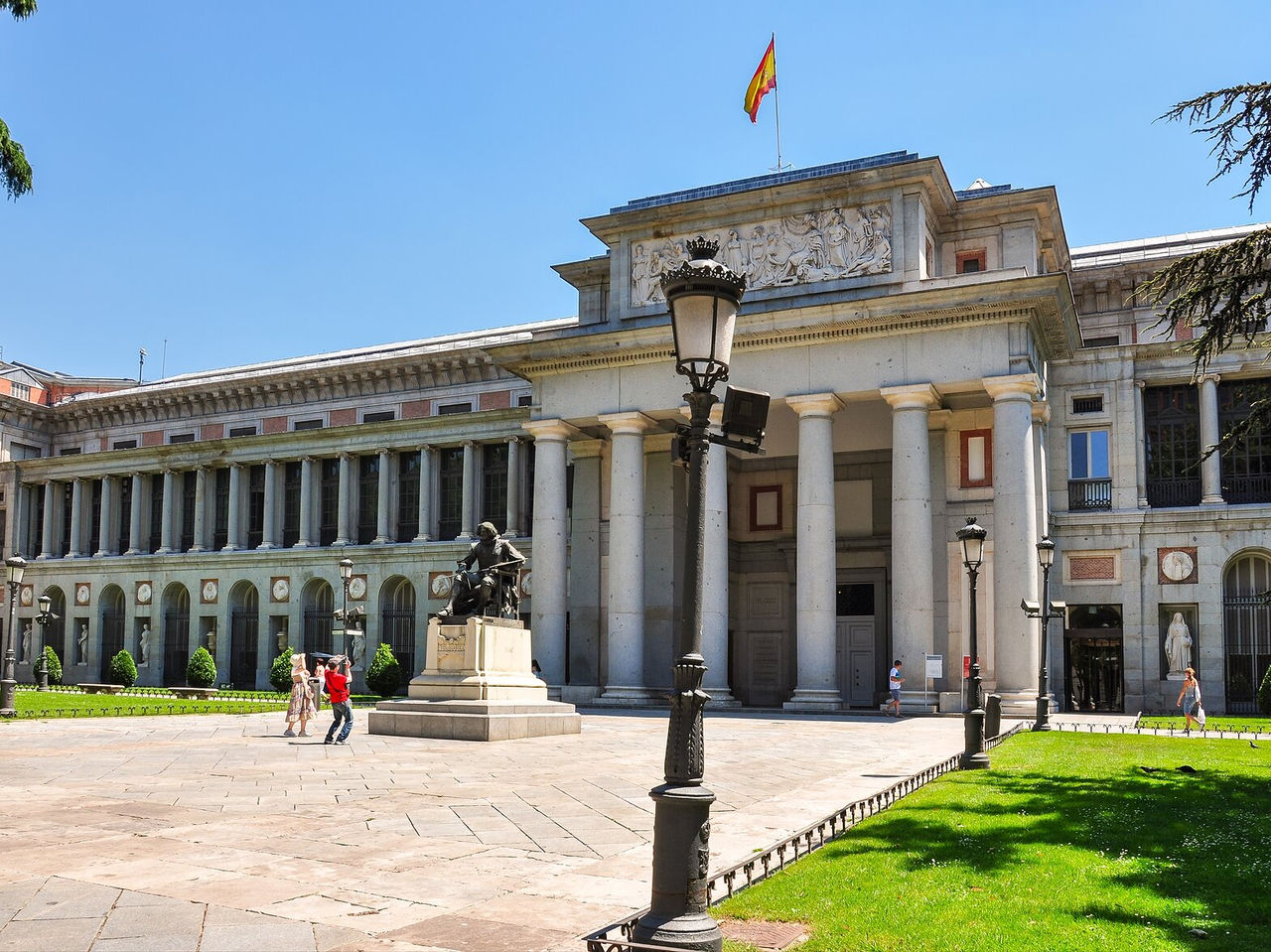 Explore Hotéis em Madrid com vista para edifício histórico de colunas clássicas e praça iluminada pelo sol