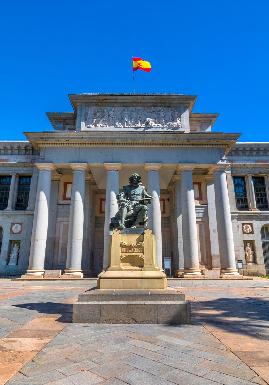 Fachada do Museu do Prado, com uma estátua na entrada e a bandeira de Espanha no cimo do edifício