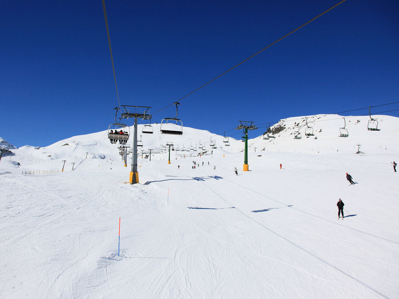 Telefericos e esquiadores numa ampla pista coberta de neve sob ceu azul intenso nas montanhas de Courmayeur