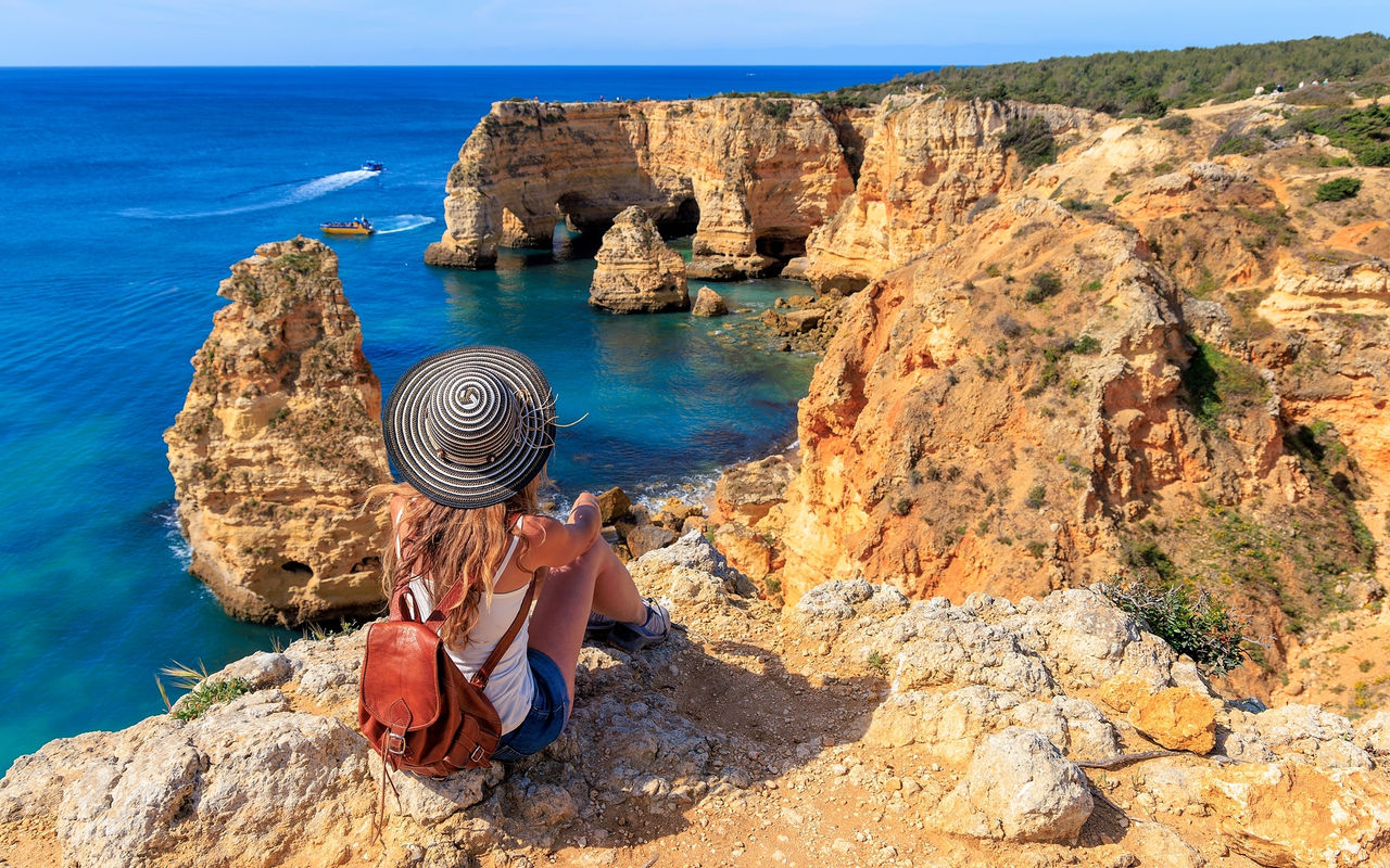 Mulher a admirar a vista panorâmica da costa algarvia, com as águas cristalinas e uma falésia rodeada por vegetação