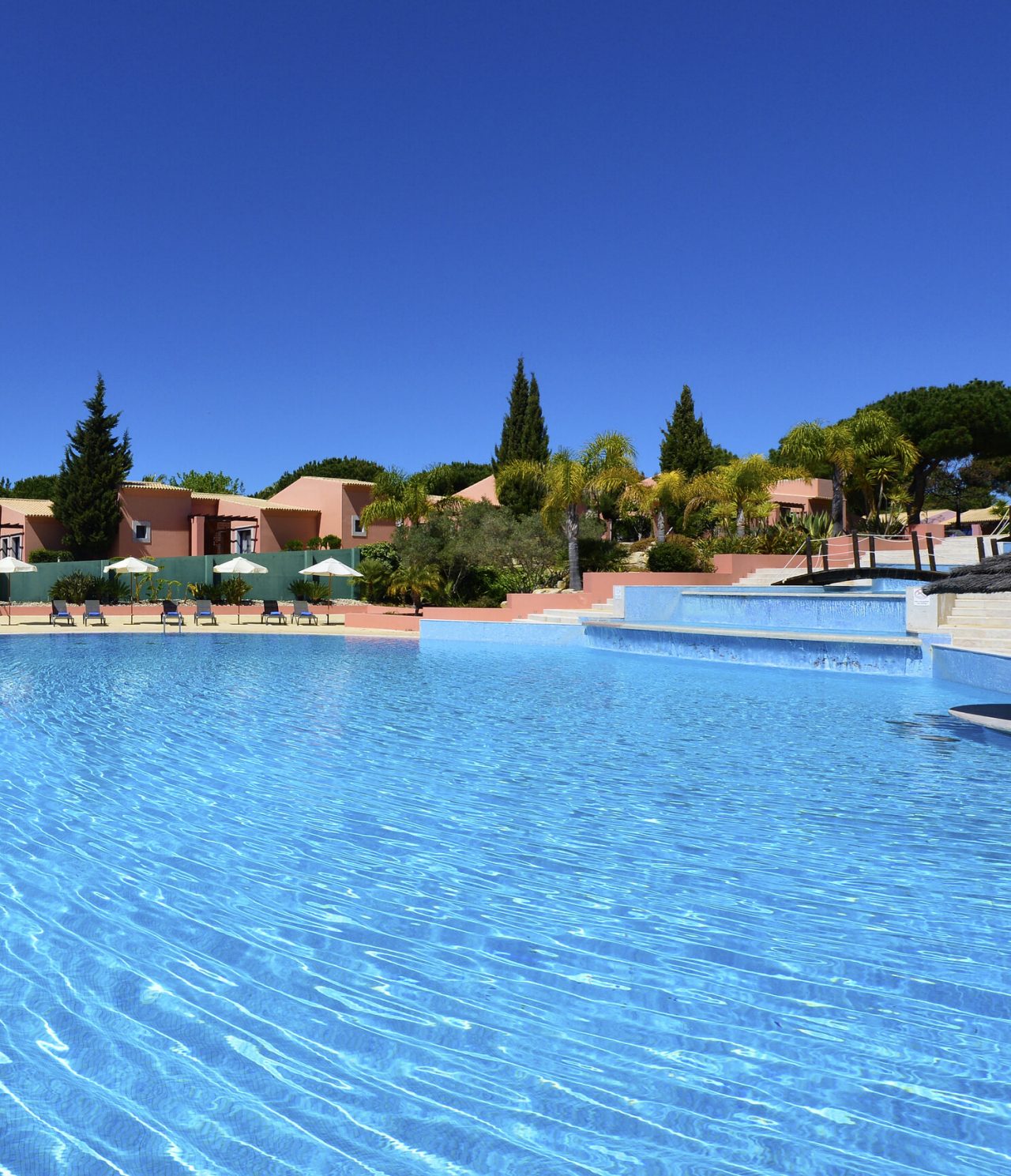 Restaurante do Pestana Vila Sol, Hotel com Golfe e Spa no Algarve, com vista para piscina azul rodeada por palmeiras e espreguiçadeiras sob céu limpo