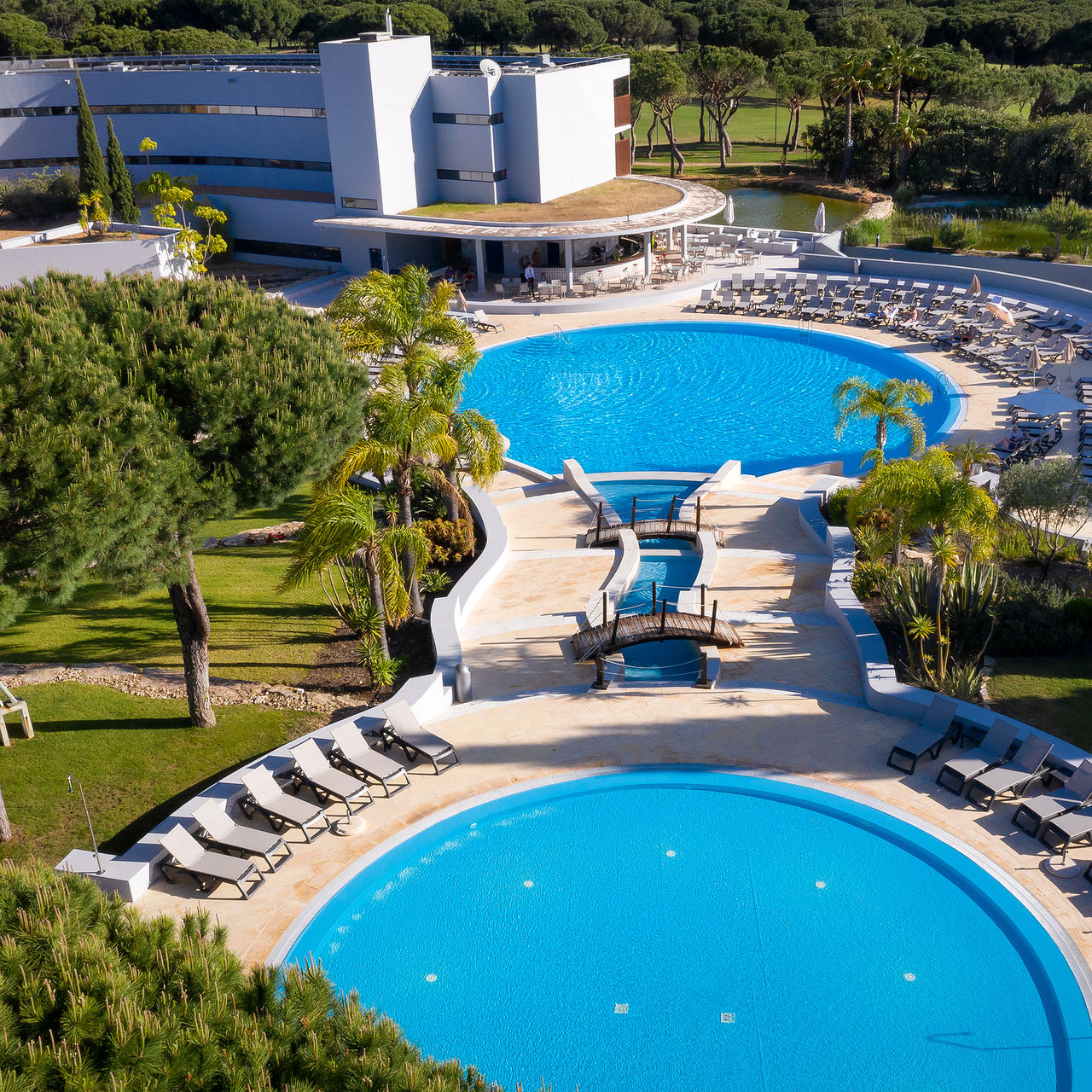 Vista aérea do Pestana Vila Sol, Hotel com Golfe e Spa no Algarve, mostrando piscinas circulares rodeadas por espreguiçadeiras e jardins verdes