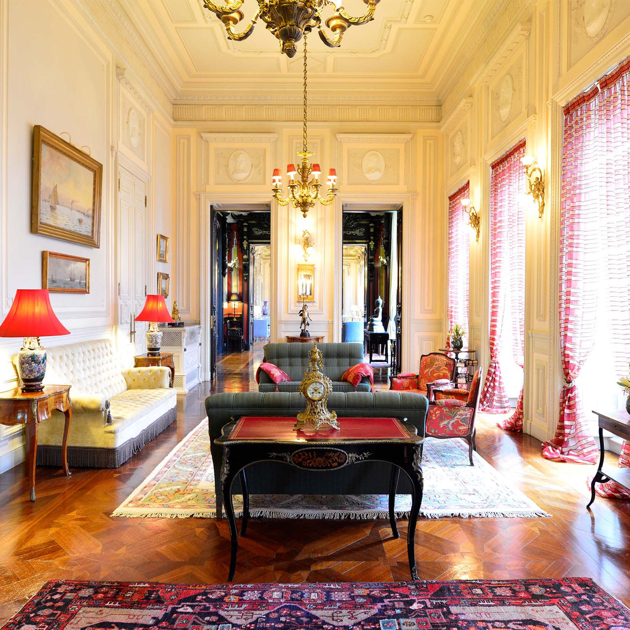 Sala do Pestana Palace Lisboa, com sofás e poltronas estofados, dois lustres dourados e paredes com painéis de madeira
