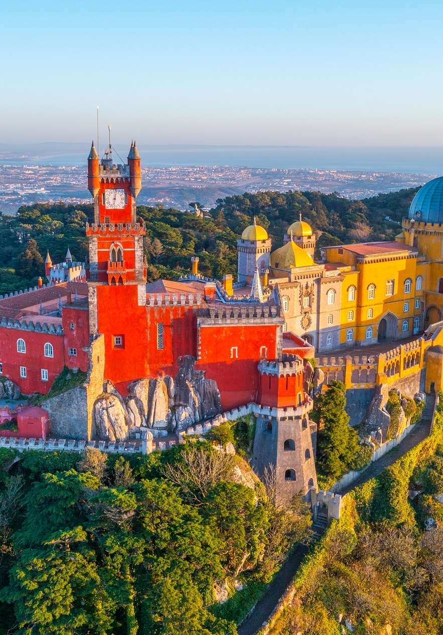 Vista panorâmica do Palácio da Pena em Sintra, conhecido pela sua arquitetura eclética, com cores vibrantes e cidade ao fundo