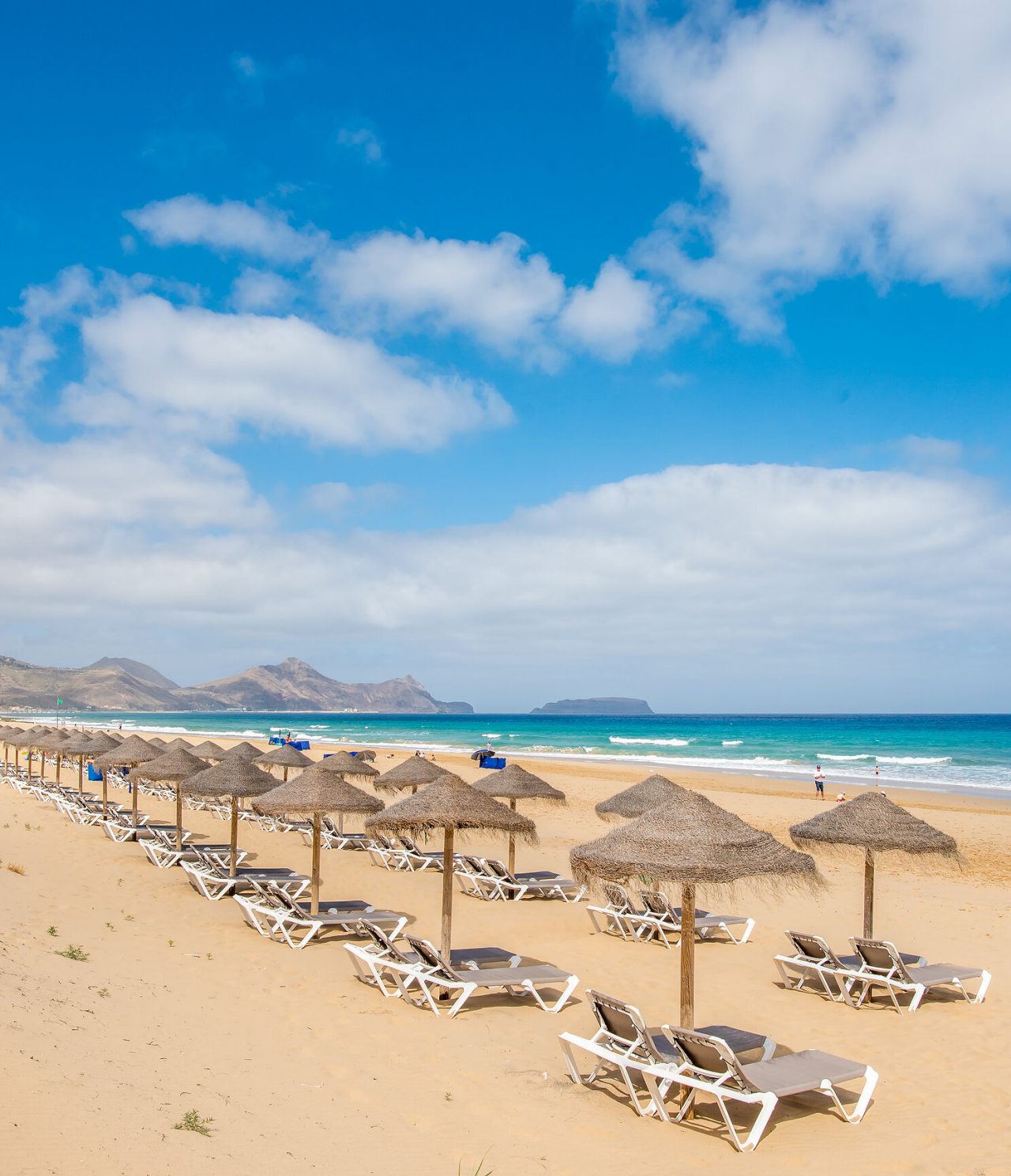 Praia de Porto Santo, com várias espreguiçadeiras e guarda sóis, com um mar azul turquesa e areia dourada