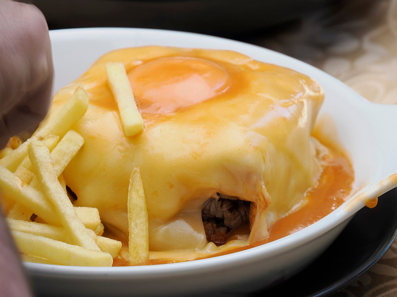 Explore Hotéis no Porto apresentando prato tradicional com queijo derretido, ovo e batatas fritas num prato branco