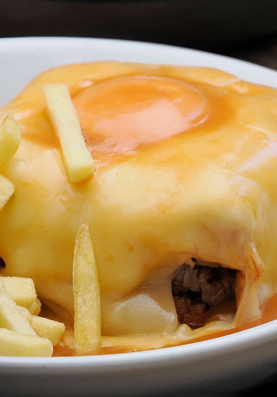 Prato tradicional de francesinha coberta com queijo derretido e ovo estrelado, acompanhado de batatas fritas, servido no Pestana Palácio do Freixo, Hotel no Rio Douro com Spa e Piscina