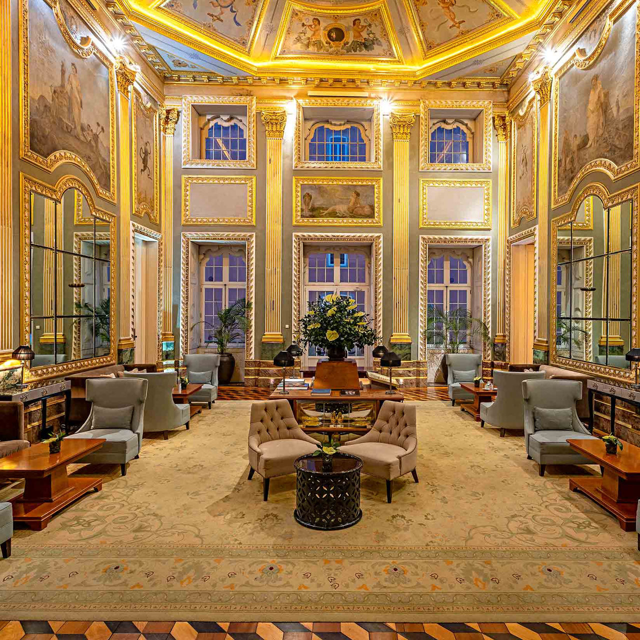 O Pestana Palácio do Freixo, Hotel 5 Estrelas no Porto, Monumento Nacional, apresenta um salão elegante com tetos altos, decoração dourada, pinturas murais e mobiliário clássico disposto em torno de mesas e poltronas confortáveis