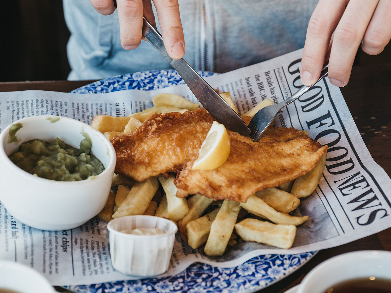 Pessoa a comer um prato típico da gastronomia de Inglaterra, peixe frito com batatas fritas a acompanhar