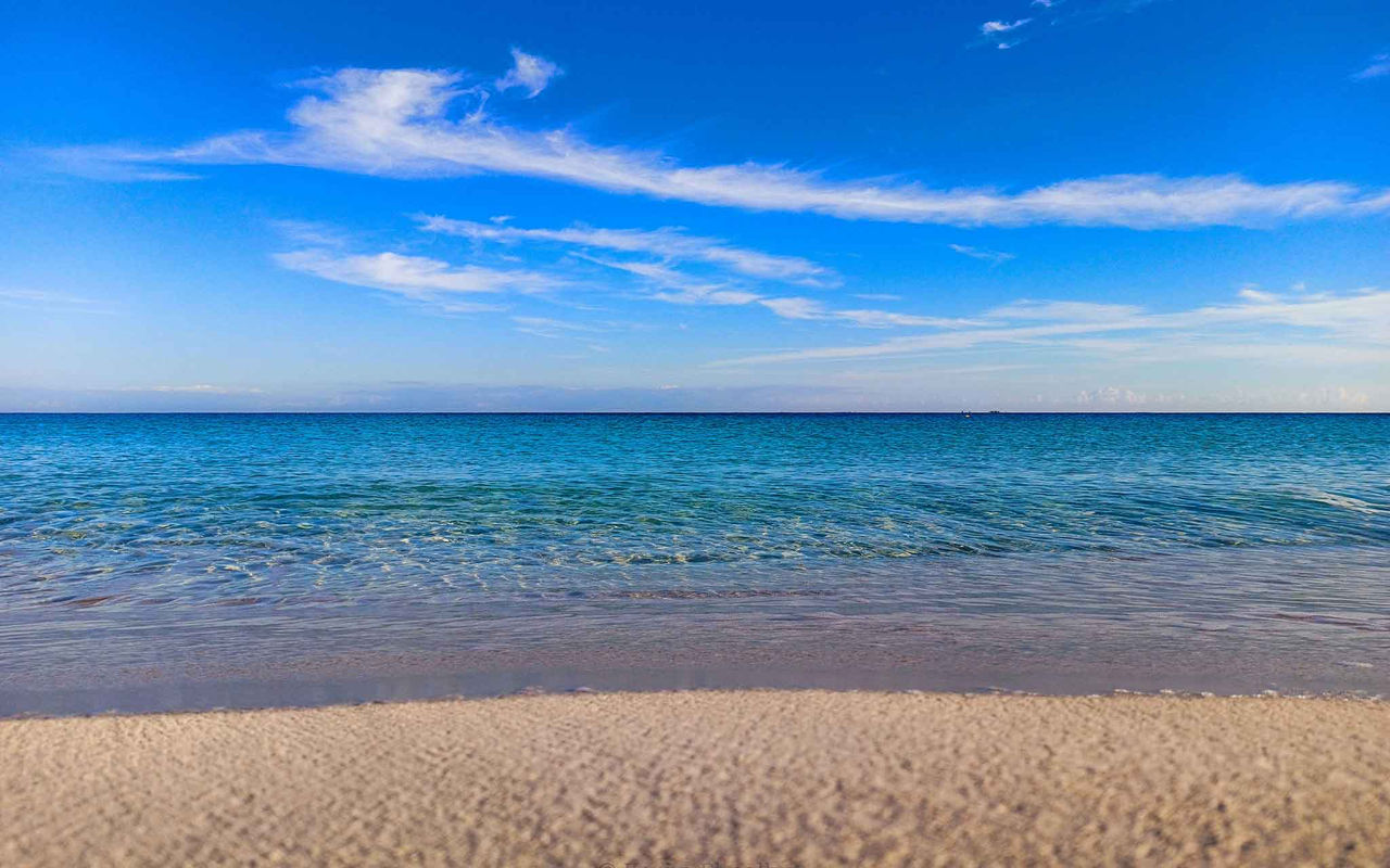 Descubra Pestana Hotel Group com vista para uma praia de areia clara, mar azul calmo e céu com nuvens leves
