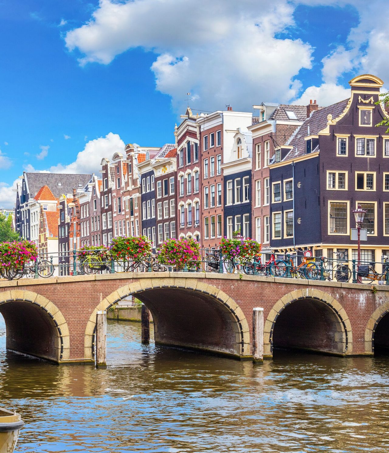 Pedestrian bridge over a canal in Amsterdam, with parked bicycles, colorful flowers, and buildings in the background