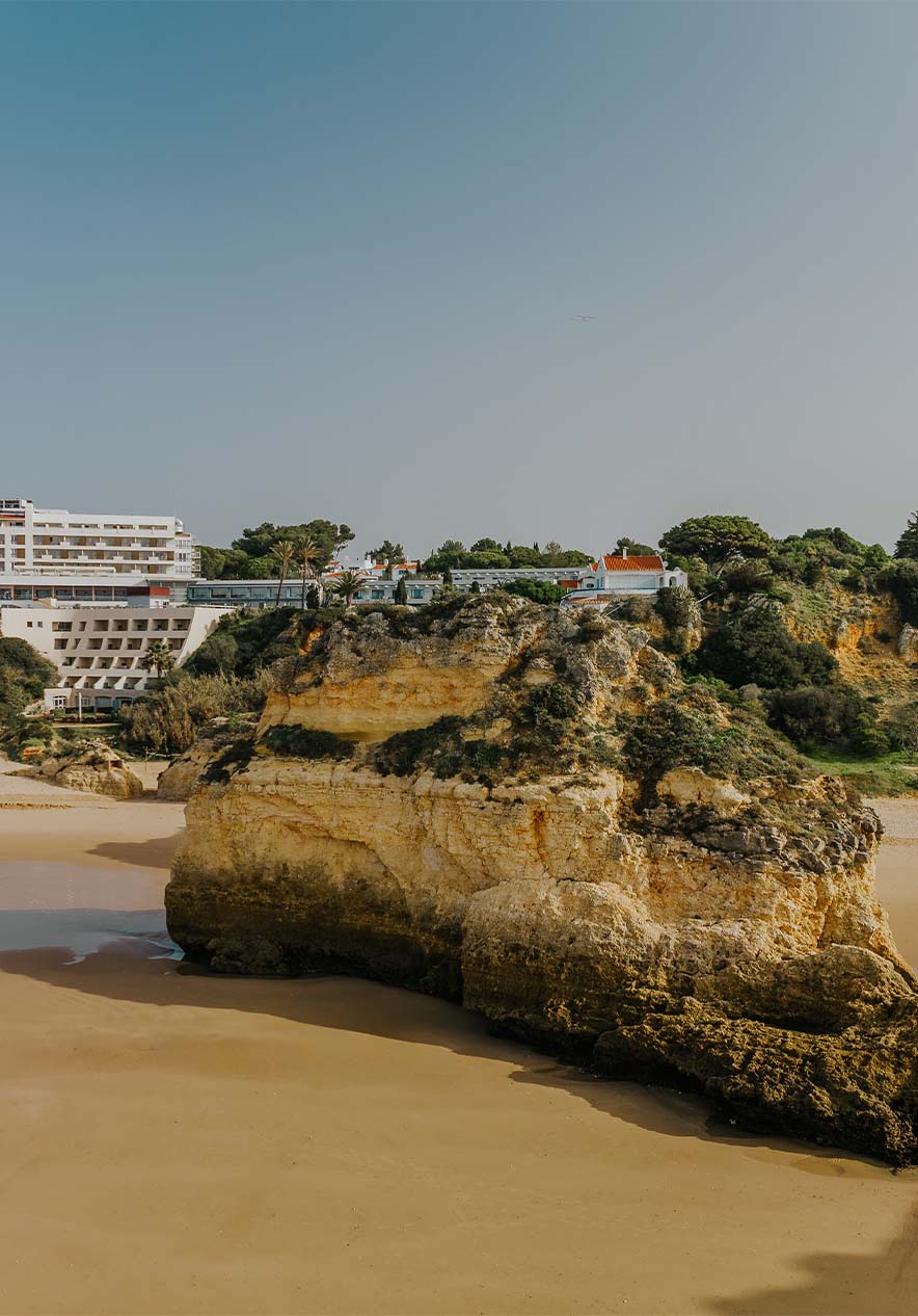 Alvor beach with rocks sand vegetation cliffs and buildings in the background under a clear sky