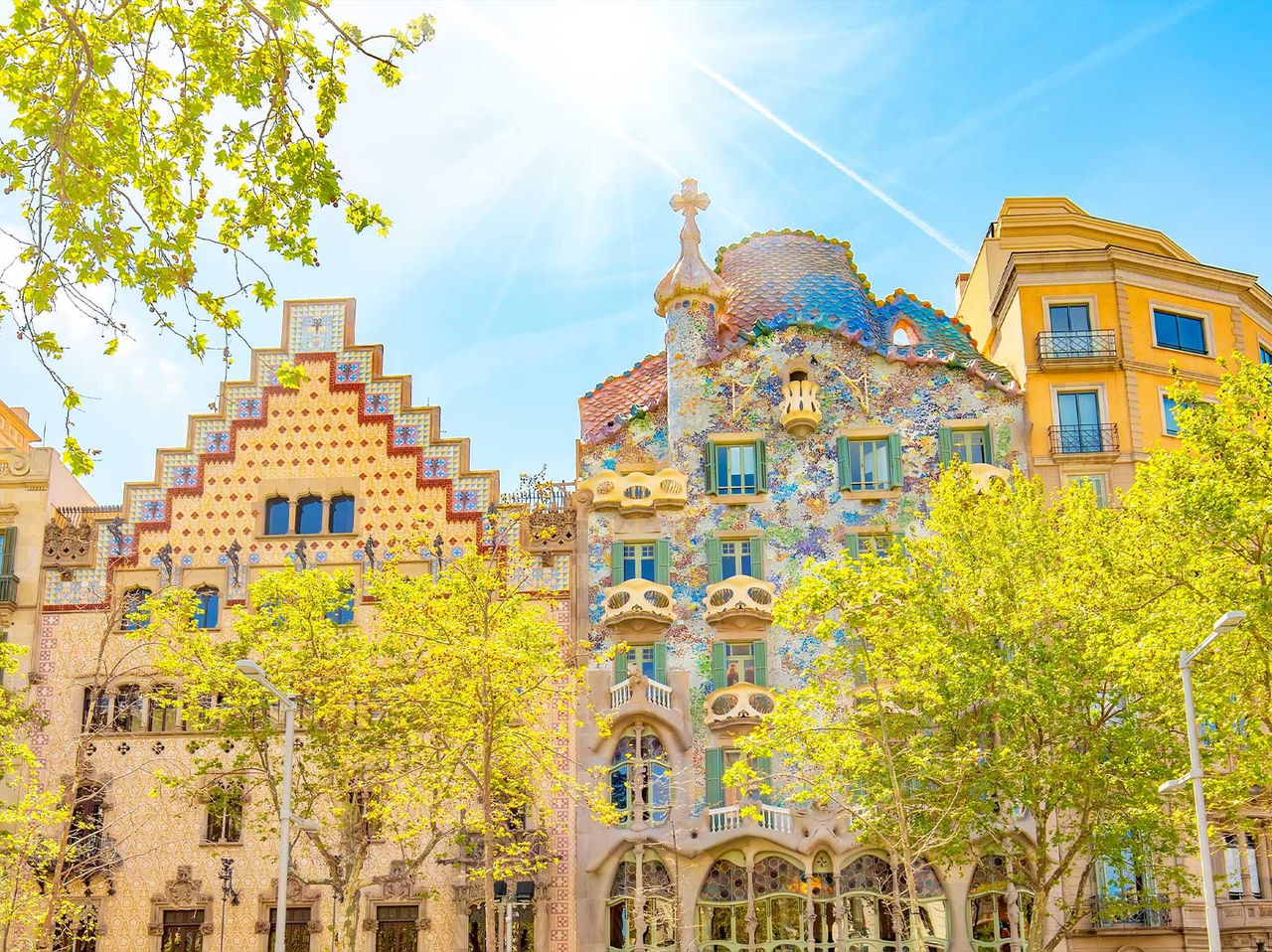 Iconic Casa Batlló building by Gaudí in Barcelona, with its colorful facade, surrounded by blooming trees