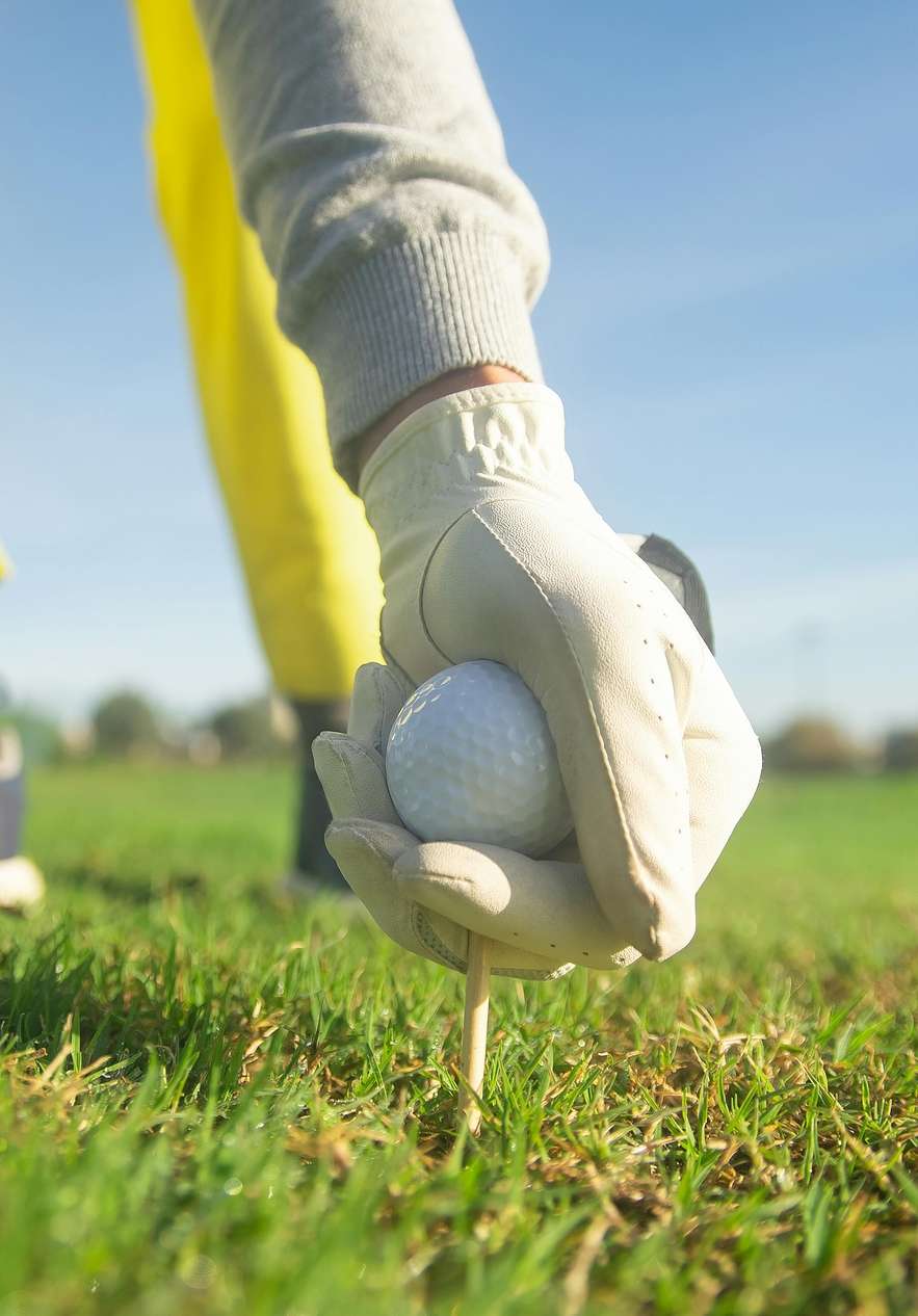 Person on a golf course placing the ball on a tee dressed in white gloves yellow pants and blue shoes