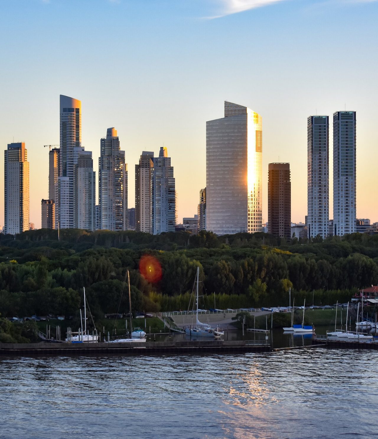 Explore Hotels in Buenos Aires featuring a riverside skyline with modern towers glowing at sunset beside moored sailboats