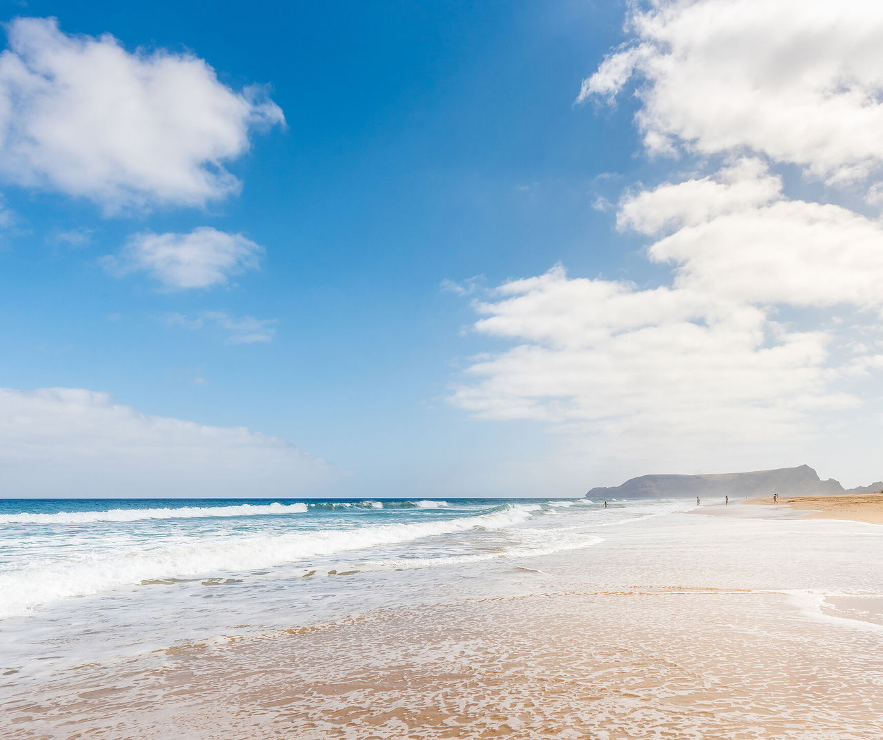 porto-santo hotel overlooking a wide sandy beach with rolling waves beneath bright clouds and distant cliffs