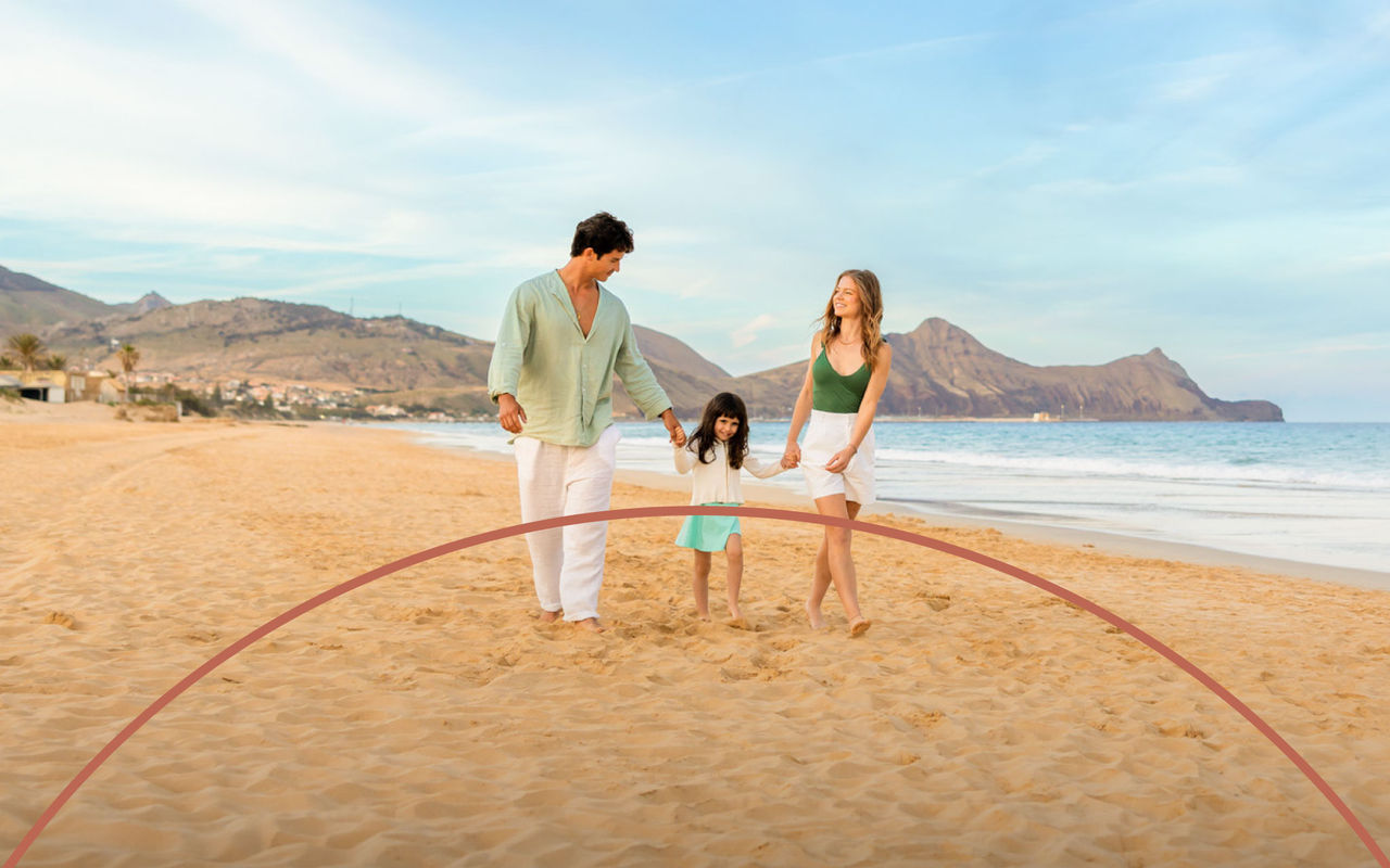 Family walking hand in hand along a sandy beach with calm sea, mountains and soft evening light under blue sky